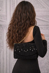 Stilvolle Frau trägt die Clutch „Königin der Nacht“ aus schwarzem Alcantara, veredelt mit Paillettenspitze, Hämatit und Kristallen, elegante Designer Abendtasche mit goldener Kette und luxuriöser Ausstrahlung.